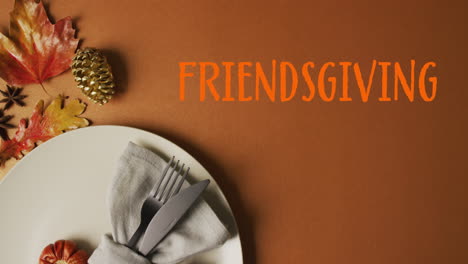 Animation-of-friendsgiving-text-over-cutlery-and-autumn-leaves-over-brown-background