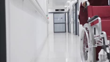 african american female doctor running with wheelchair in hospital corridor, slow motion