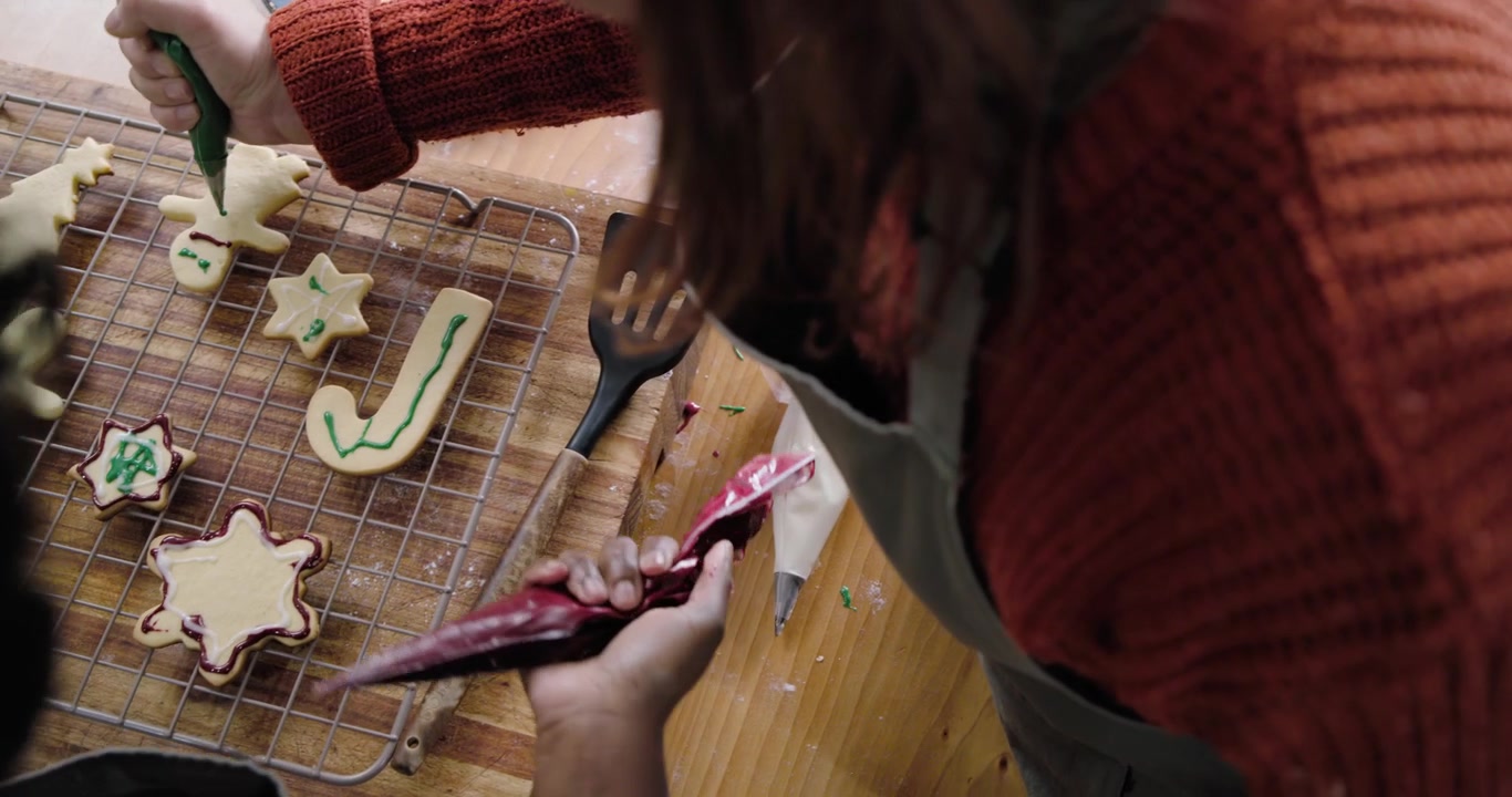 Amiche di diverse etnie che guardano una griglia di raffreddamento e decorano biscotti con sac à poche per una festa.