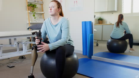 sitting on exercise ball, woman with prosthetic leg holding water bottle