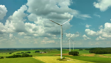 Luftaufnahmen-Zeigen-Eine-Reihe-Von-Windturbinen-Inmitten-Riesiger,-Grüner-Landwirtschaftlicher-Felder-Unter-Einem-Blauen-Himmel-Voller-Flauschiger-Wolken