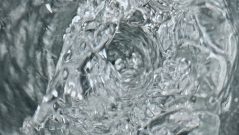 water swirling transparent glass top view. liquid vortex with bubbles closeup