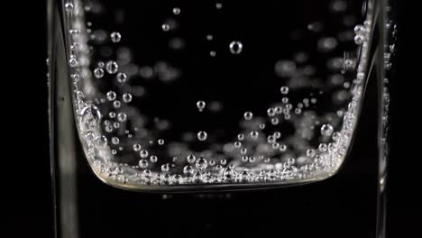 close up of mineral water bubbles in the glass. macro shop of carbonated fresh sparkling drink with oxygen balls on dark background