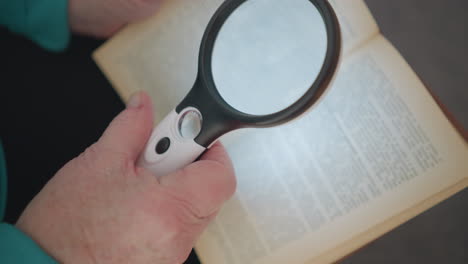 close-up of elderly person holding magnifying glass and reading book. focus on magnifying glass illuminating text, highlighting effort to read fine print, soft lighting, and relaxing indoor atmosphere
