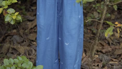 close-up of female model wearing loose blue trousers in a forest, in slow motion