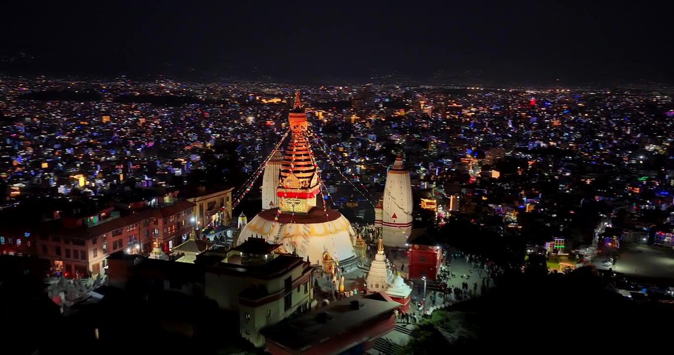 Kathmandu, Nepal, drone shot over the hilltop Swayambhunath Monkey Temple displaying the illuminated stupa and shrine complex overlooking the sparkling city lights during Tihar.