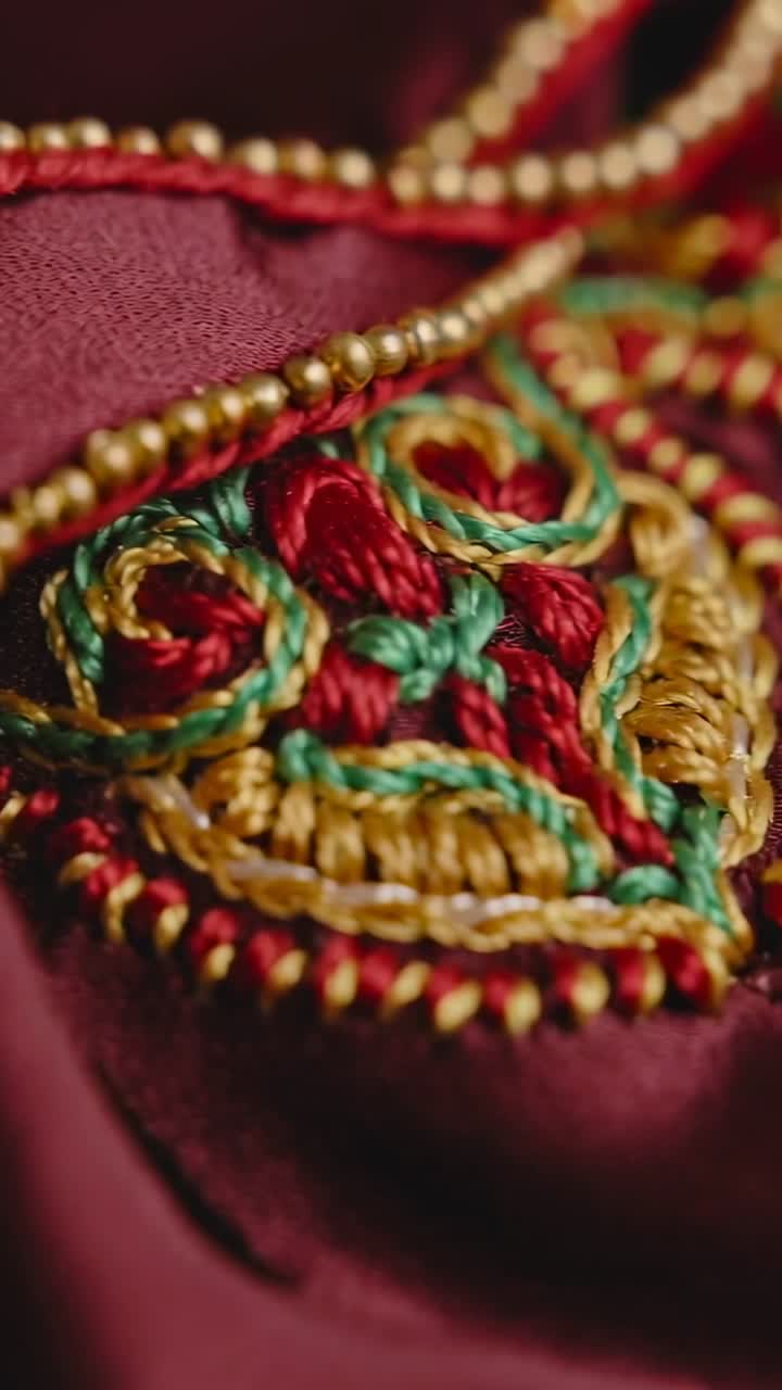 Vertical video: Focusing camera sliding over textile in studio, showing gold beads and thread motif