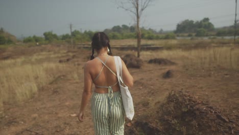 El-Primer-Plano-De-Una-Mujer-Bonita-Vestida-De-Verde-Y-Blanco-Camina-En-Cámara-Lenta-A-Través-De-Campos-Iluminados-Por-El-Sol-Con-Un-Lago-En-Segundo-Plano.