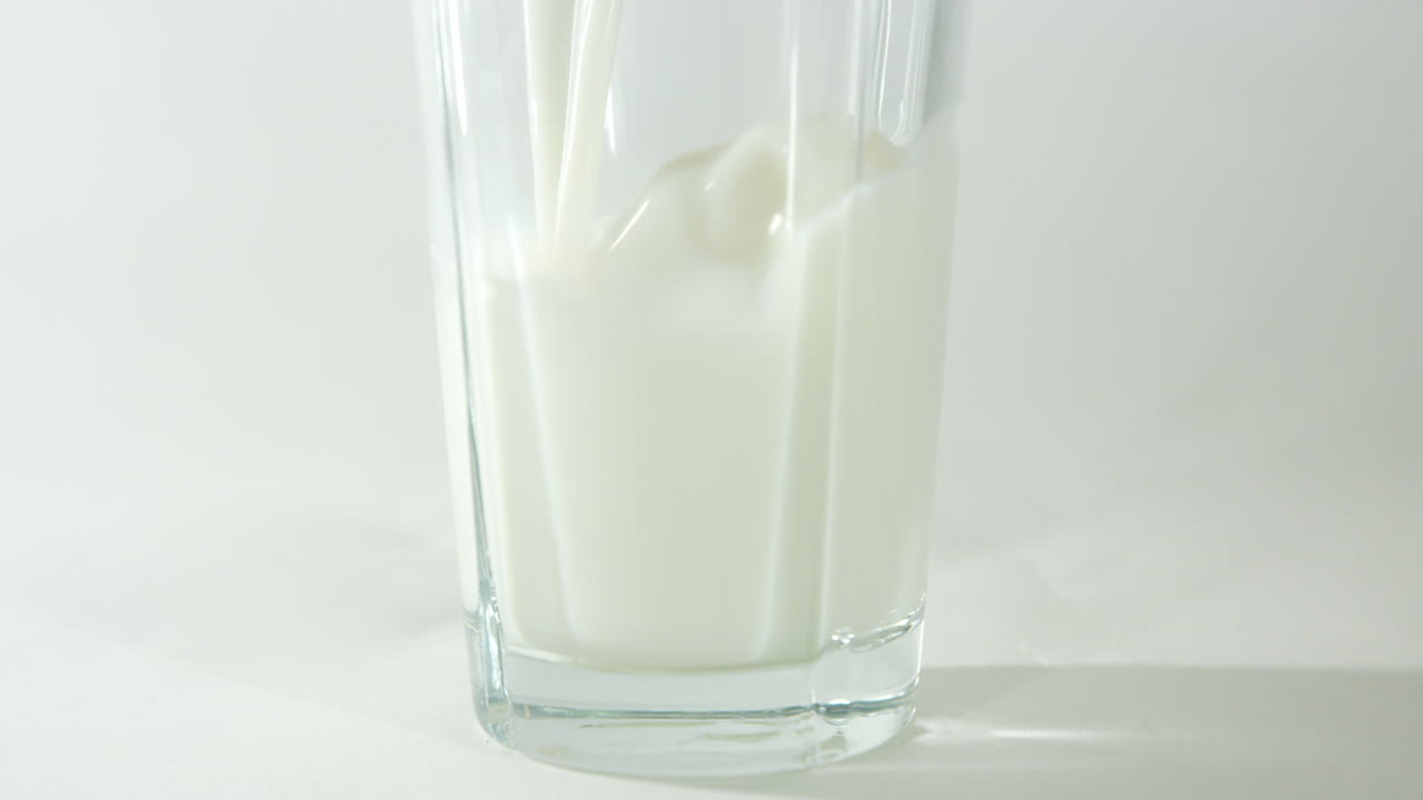 cierre en cámara lenta de la leche que se vierte en un vaso, que muestra la sección inferior del vaso con un fondo claro y claro