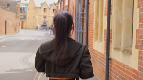 rear view of young woman exercising running along urban street wearing wireless earbuds before resting 1