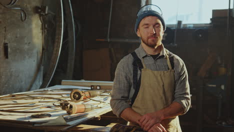 portrait of professional blacksmith by table with tools in workshop