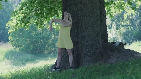 woman in yellow dress dancing by tree in summer park