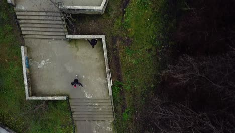 Direkte-Luftdrohnenaufnahme-Von-Zwei-Parkour-Freerunnern,-Die-Treppen-Hinunterflippen