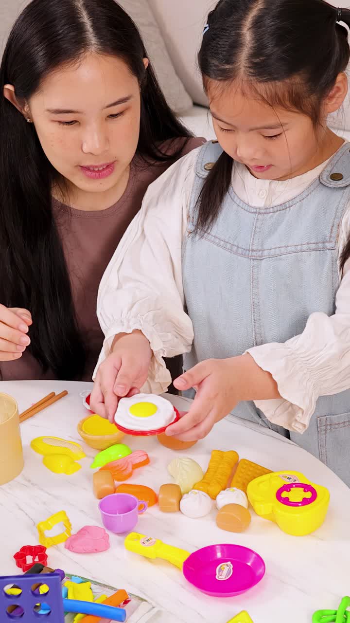 明るく居心地の良いリビングルームで、アジア人の母と娘がカラフルなおもちゃの食べ物を通して絆を深めています。