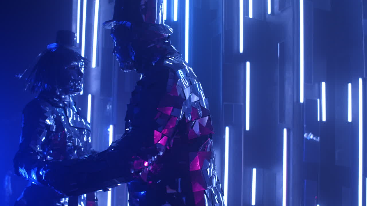 사랑에 빠진 은색 의 사람들이 함께 춤을 추고 네온 조명 속에서 회전합니다. 의상을 입은 금속 사람들이 춤을 춘다.