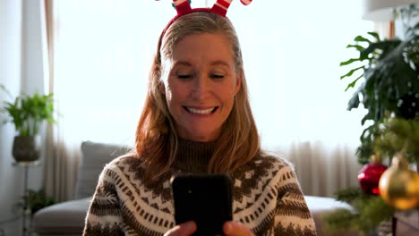 at christmas, smiling senior woman wearing festive headband using smartphone at home