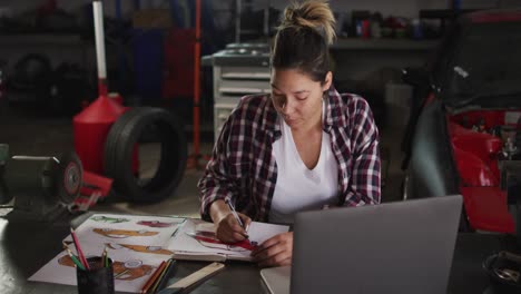 female mechanic taking notes and using laptop at a car service station