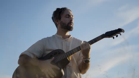 Man playing acoustic guitar in a field at sunset