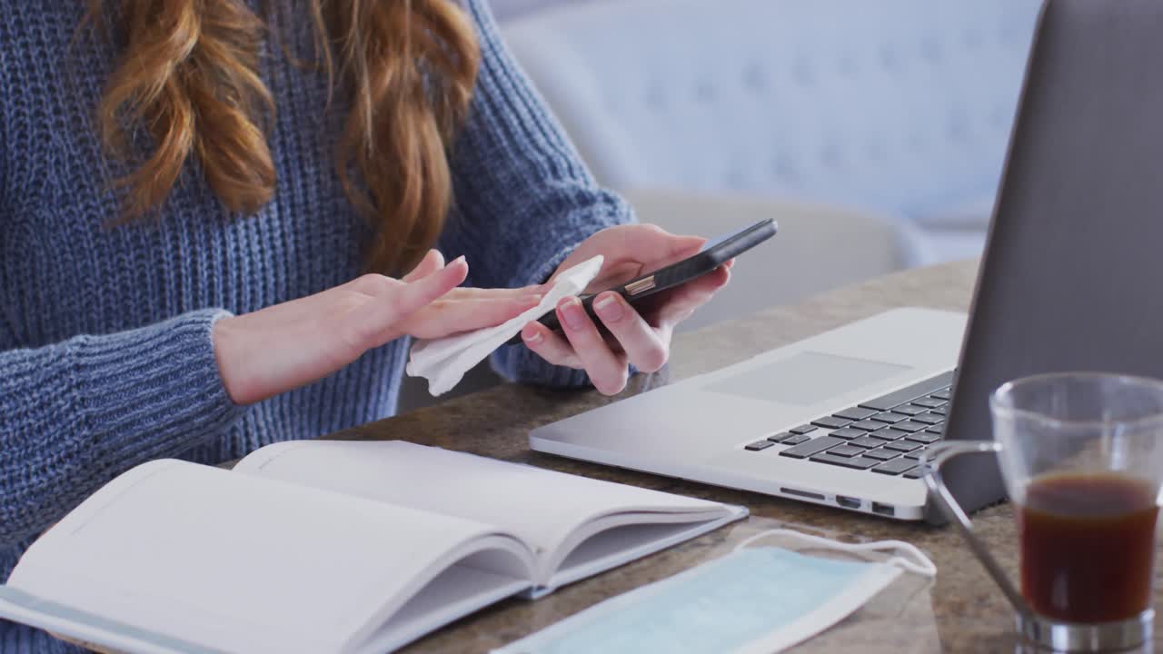 sección media de la mujer limpiando su teléfono inteligente con un pañuelo