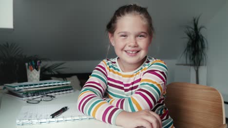 Portrait-of-cheerful-elementary-age-girl-studying-at-the-desk.