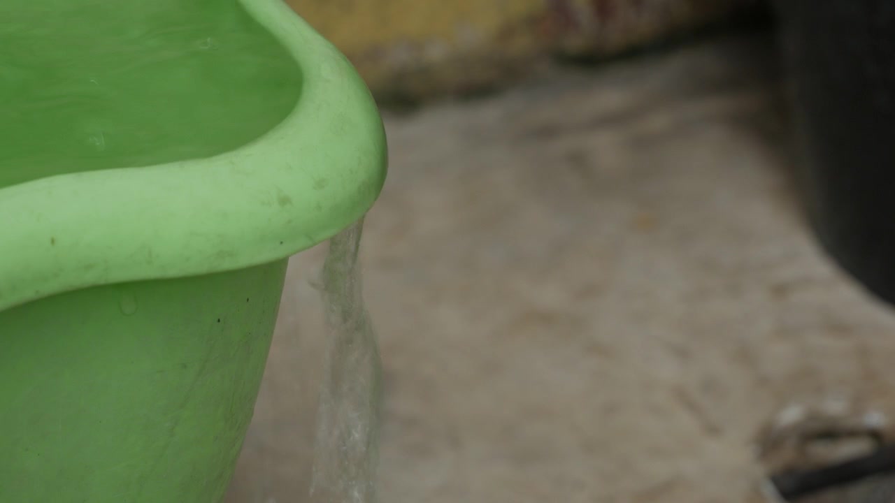 Water Overflowing from the Rim of a Full Plastic Bucket Close Up