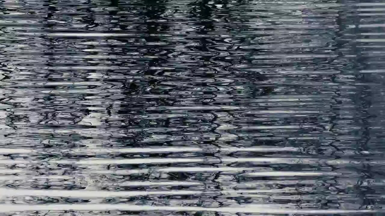 Dark rippled water surface with distorted black and white reflections, creating an abstract natural texture and moody background pattern.
