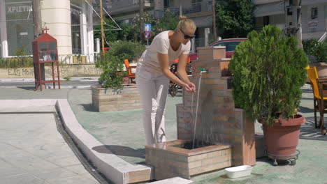 on street in city of perea greece young girl comes to the faucet and washes her hands