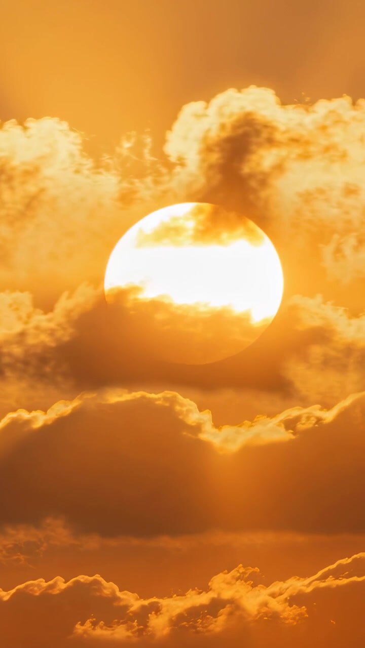 Vertical video: Drifting clouds briefly obscuring centered Sun in warm sky, producing glowing rays