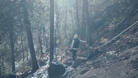 Tired-Female-Hiker-Stopped-On-Steep-Slope-While-Holding-On-Rope-Line-Tied-From-Tree-To-Tree-In-Saint-Come,-Quebec,-Canada