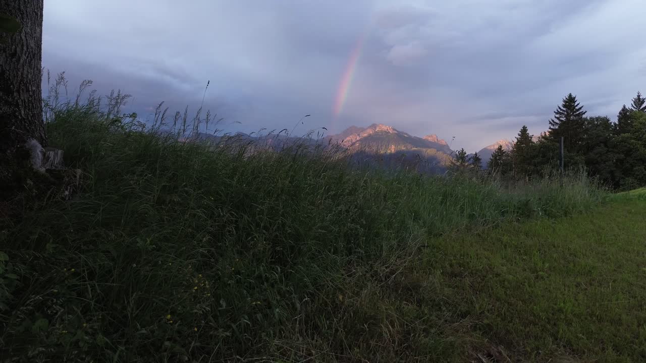 Drone rise above field reveal Mountain Landscape in Austria with Rainbow in Background