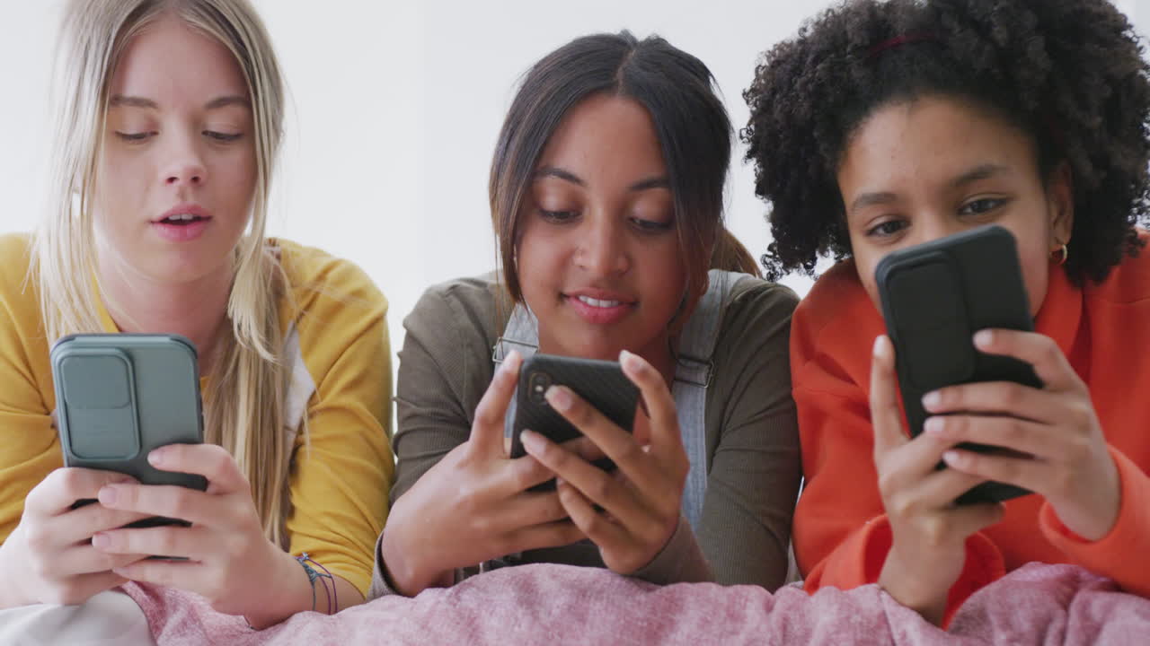 felices adolescentes diversas amigas acostadas en la cama y usando teléfonos inteligentes, cámara lenta
