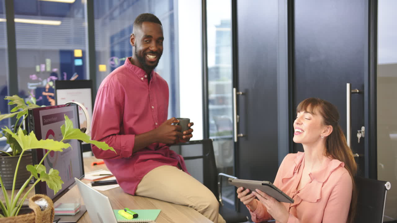 Smiling diverse colleagues in modern office, man holding coffee and woman using tablet