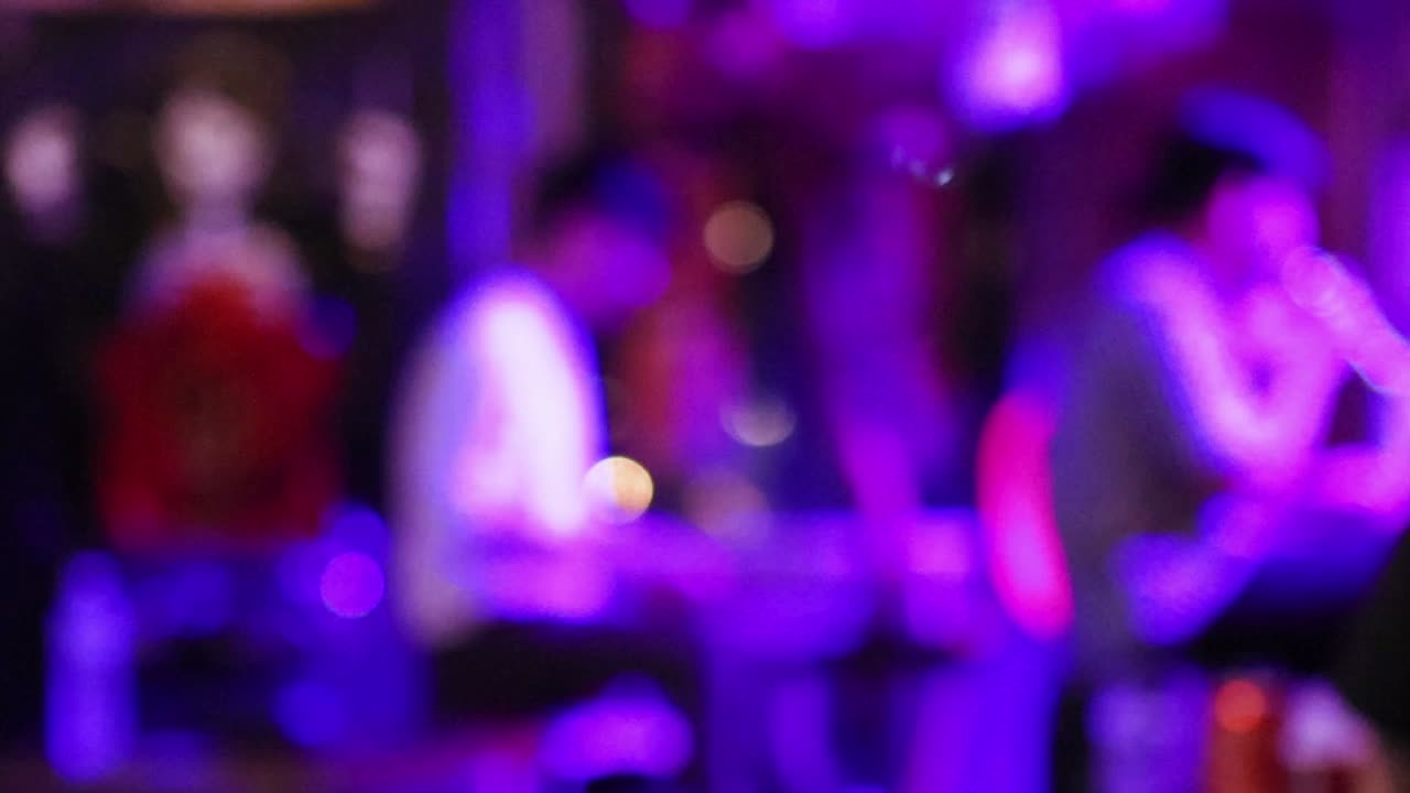 紫、赤、緑の照明が変化するステージで、焦点が合っていないミュージシャンが演奏している。