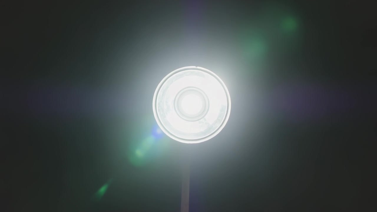 Zoomende kamera filmer cirkulær lampe på stilk over nattehimlen, viser glorie og grønblå linseflare