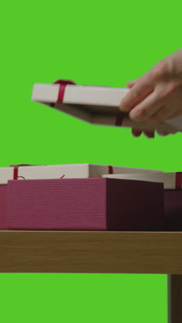 vertical video of man putting present into gift wrapped box on table shot against green screen 1