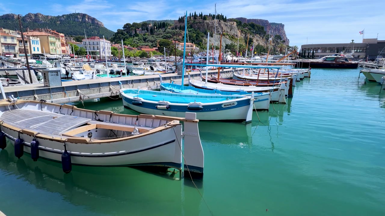 Ampia inquadratura statica di barche colorate ormeggiate in un soleggiato porto turistico mediterraneo con colline costiere.