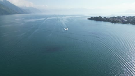 Drone-view-in-Guatemala-flying-over-a-boat-on-a-blue-lake-with-green-mountains-on-the-side-on-a-sunny-day-in-Atitlan