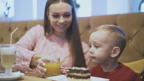 little boy eats cake and talks to mother at wooden table