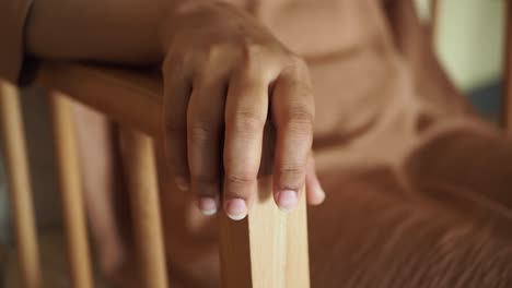 close-up of a woman's hand resting on a wooden chair armrest