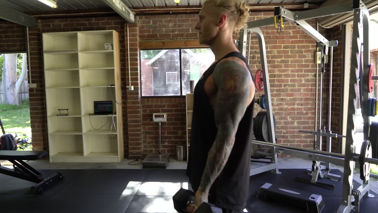 이두박근을 하는 가정 체육관에서 문신 남자 근육은 엄격합니다.