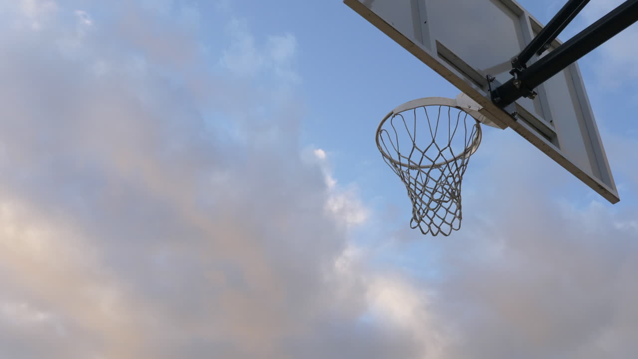 toma de acción de baloncesto pasando por un aro de baloncesto y una red contra el cielo azul