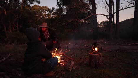 a slow motion shot of a fire crackling out in the australian bush with a bushman and his son sitting around the fire.