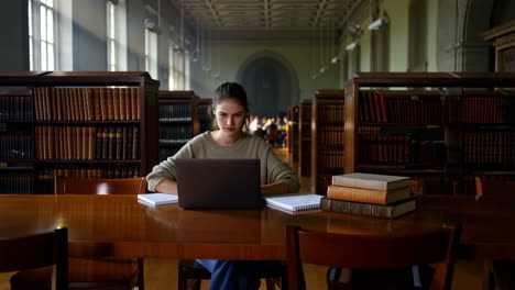 young woman studying with a laptop in a grand library