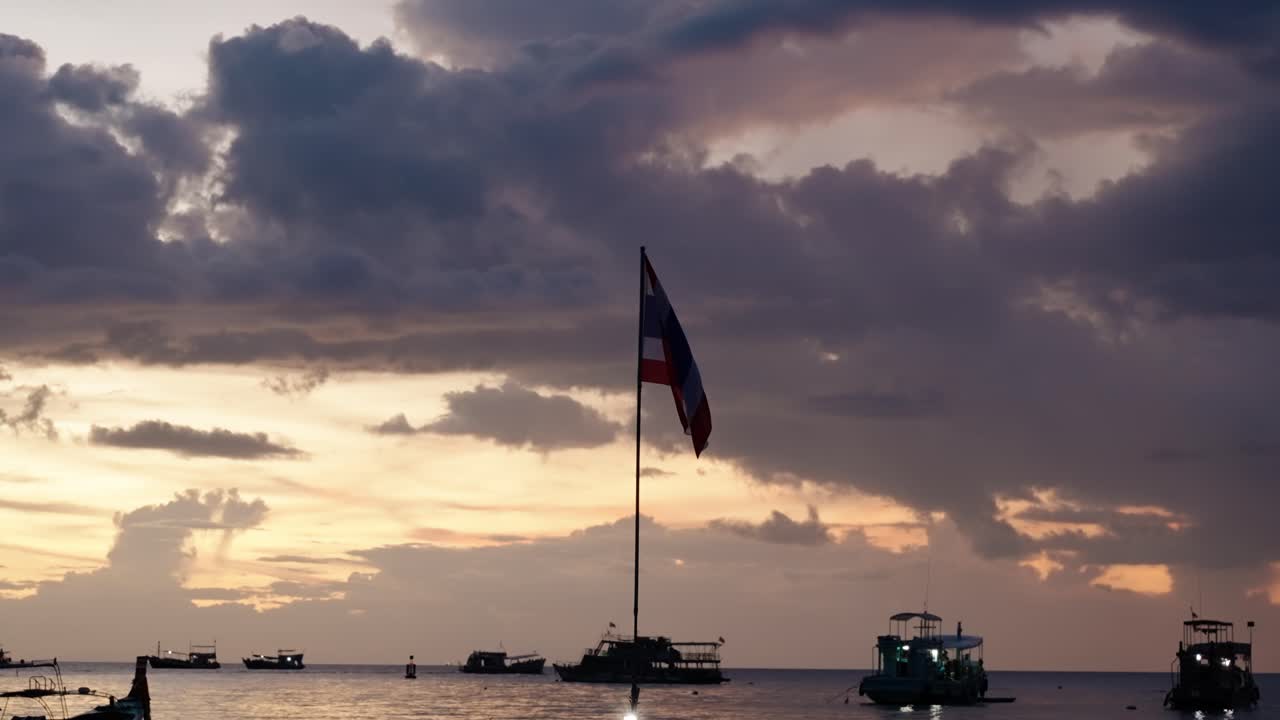 Thai flag stands tall at sunset in Ko Tao, Thailand, with boats on the horizon