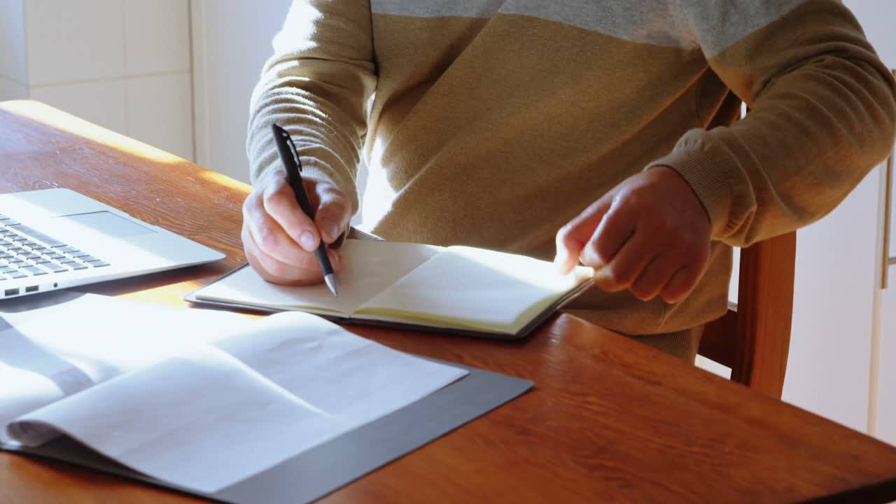 Uomo anziano che scrive sul diario in cucina 4k