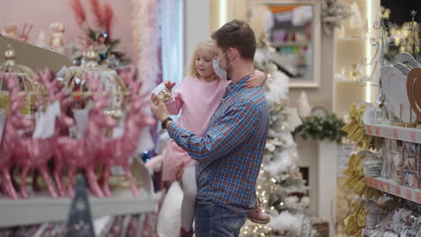 a father in a medical mask on his face with his daughter choose jewelry and toys on christmas eve to decorate the house and the christmas tree in slow motion.