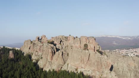 An-aerial-tilt-and-reveal-shot-of-a-village-behind-the-Belogradchik-Rocks,-a-stunning-natural-phenomenon-in-Bulgaria-with-an-intriguing-geological-history-at-the-foothills-of-the-Balkan-Mountains