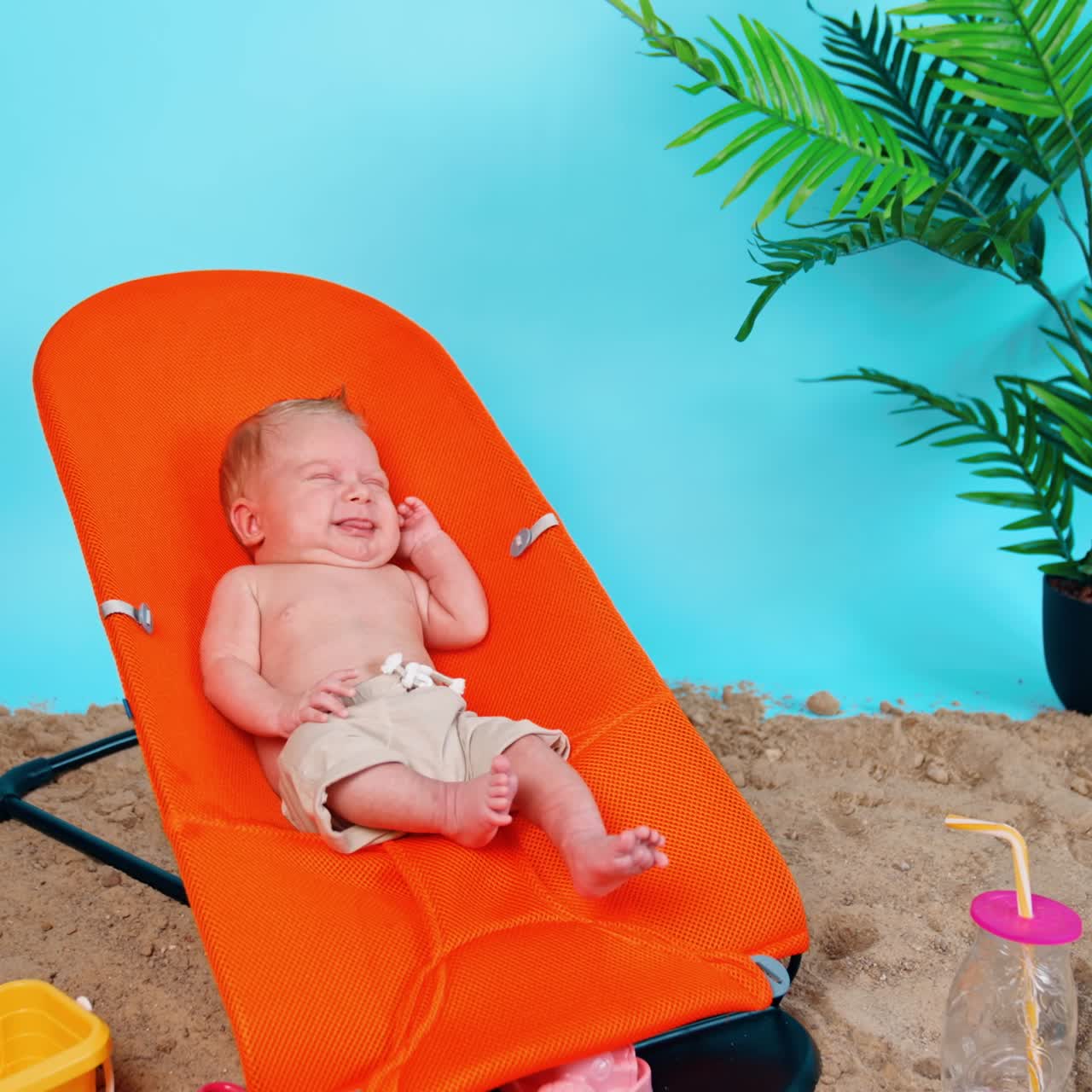 Happy little infant stretching in the orange baby chair. Newborn kid resting on the imitated beach