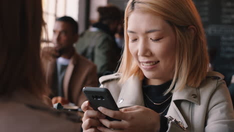 Hermosa-Mujer-Asiática-Usando-Un-Teléfono-Inteligente-En-Un-Café-Enviando-Mensajes-De-Texto-Compartiendo-Mensajes-En-Las-Redes-Sociales-Disfrutando-De-La-Tecnología-Móvil-Esperando-En-Un-Restaurante-Concurrido