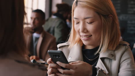 hermosa mujer asiática usando un teléfono inteligente en un café enviando mensajes de texto compartiendo mensajes en las redes sociales disfrutando de la tecnología móvil esperando en un restaurante ocupado